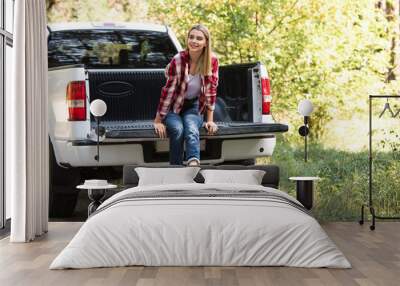 attractive young woman looking away and sitting in trunk of pick up car outdoors Wall mural