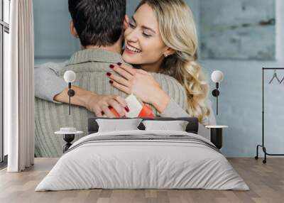 attractive young woman with gift box embracing her boyfriend at home Wall mural