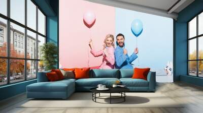 back to back view of smiling woman and handsome man with balloons showing yes gesture on pink and blue background Wall mural