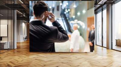 back view of bi-racial security man adjusting earpiece near blurred businesswoman and african american bodyguard. Wall mural