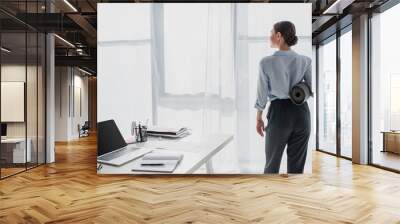 back view of businesswoman holding yoga mat at workspace with laptop and notepad Wall mural