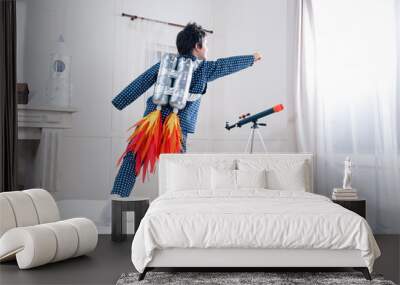 Back view of cute little boy in pajamas playing astronaut on bed Wall mural