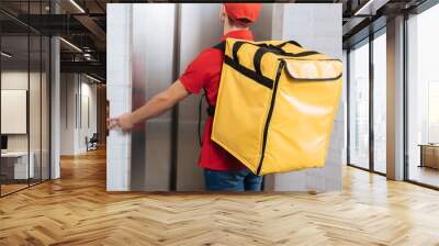 Back view of delivery man in red uniform with thermo backpack pressing elevator button Wall mural