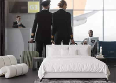 back view of male and female pilots walking by airport lobby with suitcases Wall mural