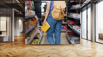 back view of student with backpack and copybook walking along racks in stationery shop. Wall mural