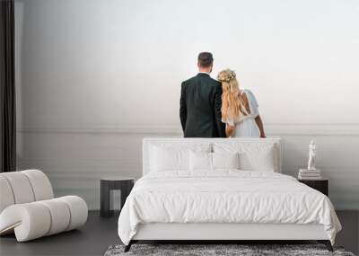 back view of wedding couple standing on beach with wedding bouquet and looking at sea Wall mural