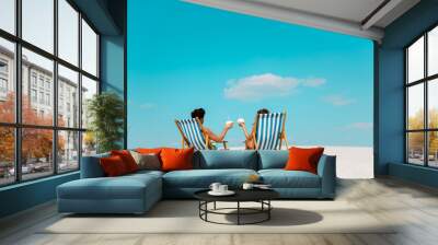 back view of young couple sitting in deck chairs with coconut drinks on sandy beach Wall mural