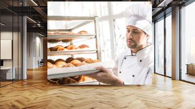 baker in chefs uniform looking at trays with fresh cooked croissants Wall mural