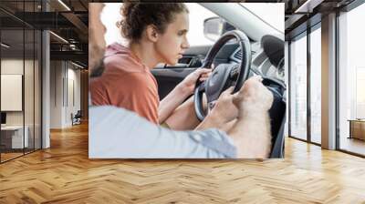 bearded father pointing at speedometer while teaching teenage son how to drive car. Wall mural