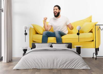 bearded latin man watching championship while sitting on sofa and celebrating triumph isolated on white Wall mural