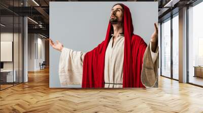 bearded man in red hood praying with outstretched hands isolated on grey Wall mural