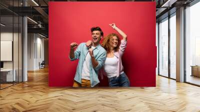 Beautiful excited couple dancing in casual clothes isolated on red Wall mural