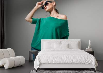 beautiful female model in sunglasses and green sweater posing isolated on grey background Wall mural