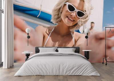 beautiful girl in swimwear and sunglasses reaching hands and smiling at camera on yacht Wall mural