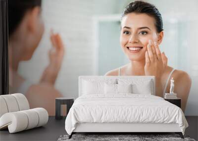 beautiful happy girl applying face cream and looking at mirror in bathroom Wall mural