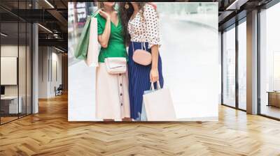 beautiful smiling girls holding paper bags and looking away while standing together in shopping mall Wall mural