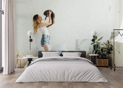 Beautiful smiling young woman holding Scottish fold cat in modern bedroom with copy space Wall mural