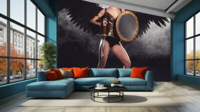 beautiful woman in warrior costume and angel wings posing with shield and sword on black background Wall mural