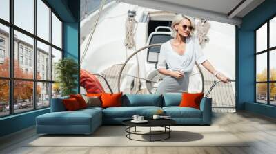 Beautiful young blonde woman in sunglasses standing on yacht Wall mural