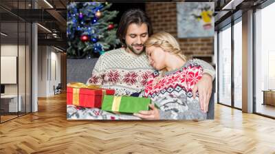 beautiful young couple holding christmas gifts and sitting together on couch Wall mural