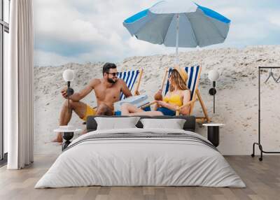 beautiful young couple with coconut cocktails relaxing in sun loungers on sandy beach Wall mural