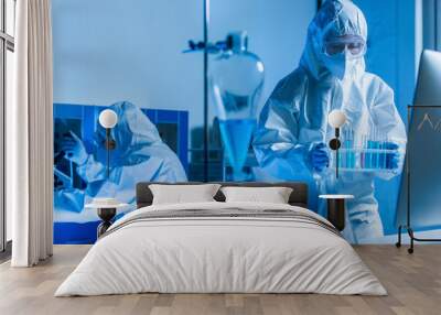 bioengineer holding test tubes while colleague working on background. Wall mural