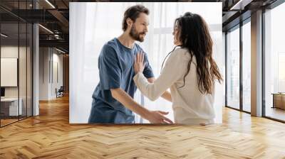 Brunette woman pushing angry boyfriend during conflict at home. Wall mural