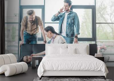 Business colleagues helping young fainted woman lying on sofa in office Wall mural