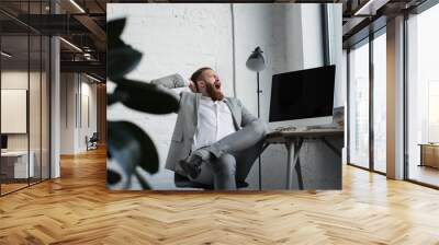 businessman yawning and sitting in chair in office Wall mural