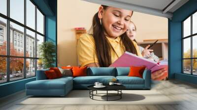 cheerful asian girl reading book near kids during lesson, banner Wall mural