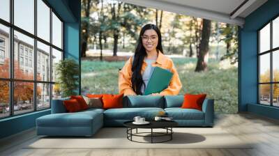 cheerful asian student with notebooks looking at camera in park Wall mural