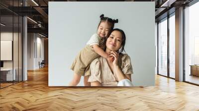 cheerful asian toddler daughter hugging happy mother isolated on gray Wall mural