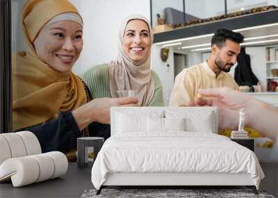 cheerful asian woman holding cup of tea during dinner with muslim family. Wall mural