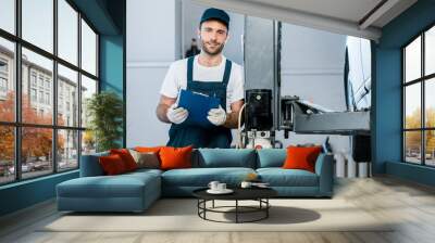 cheerful auto mechanic in cap holding clipboard in car service Wall mural