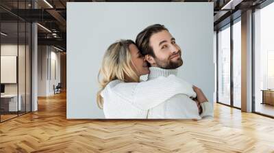 cheerful blonde woman in white knitted sweater hugging bearded man isolated on grey Wall mural