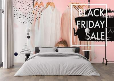 cheerful charming kid in trendy overalls sitting under clothes on hangers, black friday sale banner Wall mural