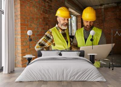 cheerful devoted construction workers in safety vests working with laptop on site, cottage builders Wall mural