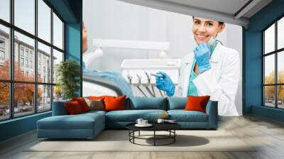 cheerful female dentist holding drill and smiling near patient Wall mural