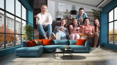 cheerful friends smiling while sitting on sofa at home and watching tv Wall mural