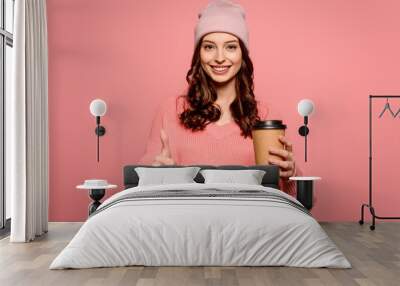 cheerful girl holding coffee to go and showing thumb up on pink background Wall mural