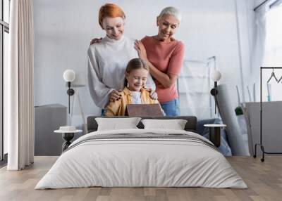 cheerful girl holding house model near same sex mothers in new home Wall mural