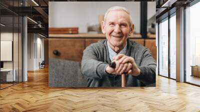 cheerful pensioner smiling and holding walking cane at home Wall mural