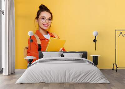 cheerful student in glasses looking at camera while holding notebook isolated on yellow Wall mural