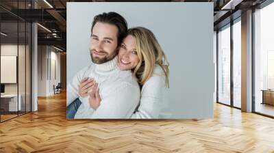 cheerful woman hugging bearded man in white sweater and looking at camera isolated on grey Wall mural