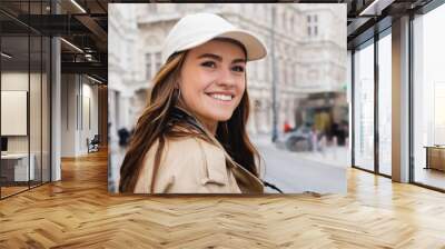 cheerful woman in trench coat and baseball cap on street of in european city, banner. Wall mural