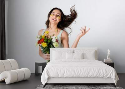 cheerful young woman with petals on face holding bouquet of flowers isolated on white Wall mural