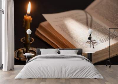 church candle in candlestick burning near bible with catholic cross in dark with sunlight Wall mural