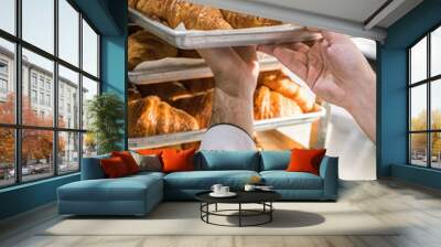 close up of male baker putting baking tray with croissants on rack Wall mural