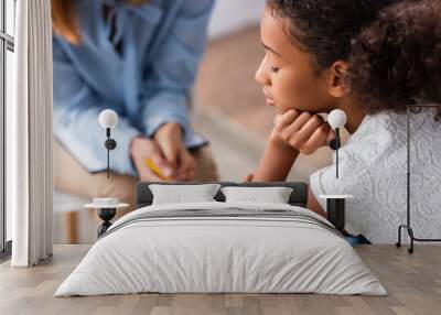 Close up of upset african american girl with closed eye near psychologist during consultation on blurred background Wall mural