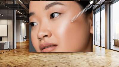 close up view of asian woman applying moisturizing cosmetic serum during facial pampering isolated on grey. Wall mural